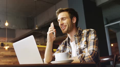 Man-talking-on-mobile-phone-while-using-laptop-in-cafe-4k