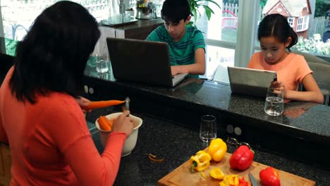 Niños-Usando-Computadora-Portátil-Y-Tableta-Digital-Mientras-La-Madre-Corta-Verduras-4k