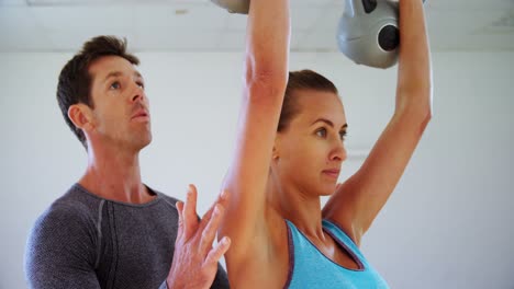 Coach-assisting-a-woman-to-exercise-with-kettlebell-4k