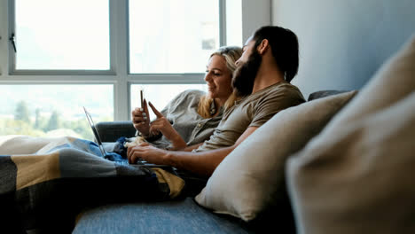 Couple-using-mobile-phone-and-laptop-in-living-room-4k