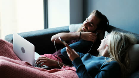 Couple-listening-music-on-mobile-phone-while-using-laptop-in-living-room-4k