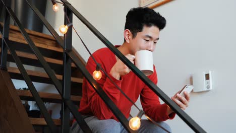 Man-having-coffee-while-using-mobile-phone-on-stair-4k