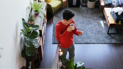 Mann-Mit-Kaffeetasse-Und-Mobiltelefon-Im-Wohnzimmer-4k