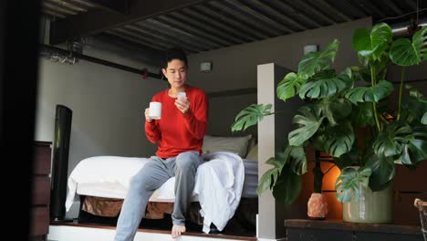 Man-with-coffee-cup-using-mobile-phone-on-bedroom-4k
