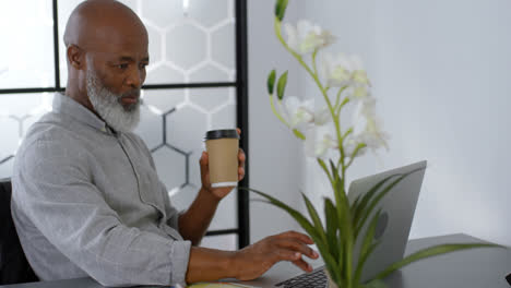 Businessman-having-coffee-while-using-laptop-on-desk-4k