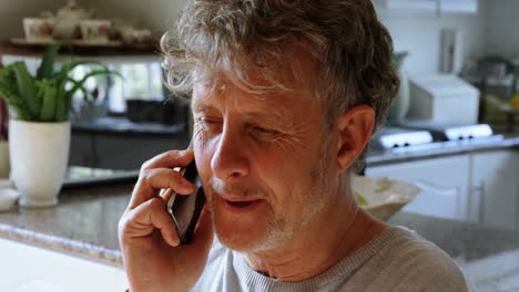 Senior-man-talking-on-mobile-phone-in-kitchen-at-home-4k