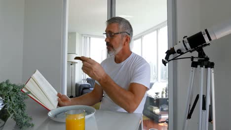 Man-reading-book-while-eating-breakfast-on-table-4k