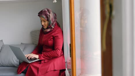 Woman-in-hijab-using-laptop-in-living-room-4k