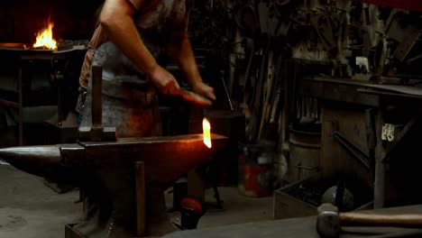 Blacksmith-examining-a-hot-metal-rod-with-brush-4k