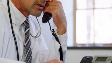 Physician-using-laptop-while-talking-on-landline-at-desk-in-clinic-4k