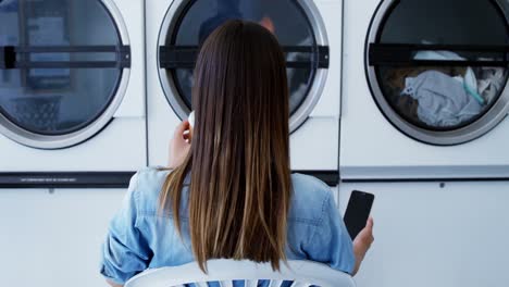 Woman-having-coffee-while-using-mobile-phone-at-laundromat-4k