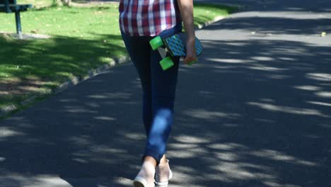 Woman-with-skateboard-walking-on-street-near-park-4k