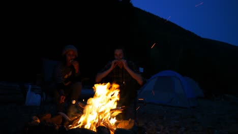 Hiker-couple-eating-food-near-campfire-4k