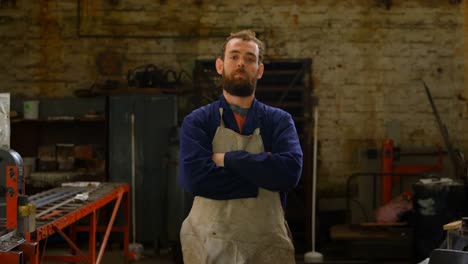 Metalsmith-standing-with-arms-crossed-in-workshop-4k
