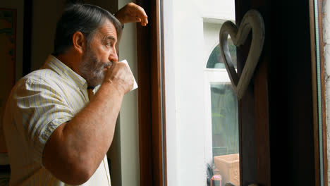 Senior-man-looking-through-window-while-having-coffee-at-home-4k