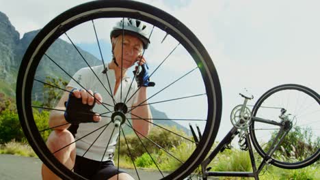Senior-cyclist-repairing-bicycle-while-talking-on-mobile-phone-4k