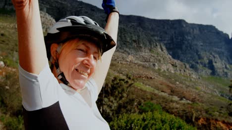 Senior-cyclist-standing-with-arms-up-at-countryside-4k