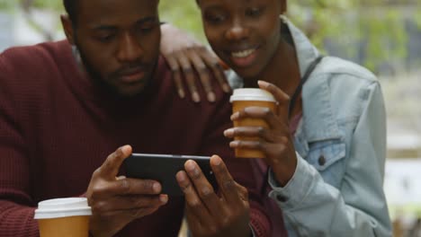 Couple-using-mobile-phone-while-having-coffee-in-outdoor-cafe-4k