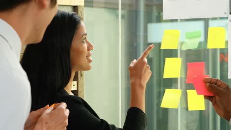 Executives-discussing-over-sticky-note-on-glass-wall-4k