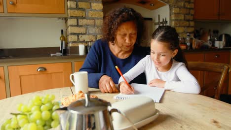 Grandmother-helping-granddaughter-in-studies-in-kitchen-4k