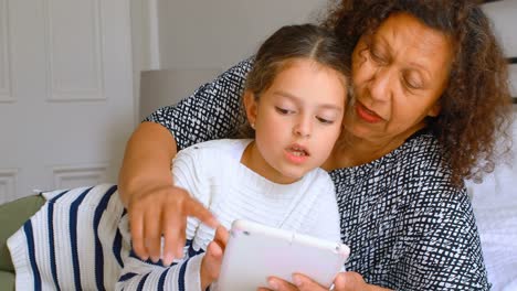 Girl-using-digital-tablet-with-grandmother-in-bedroom-4k