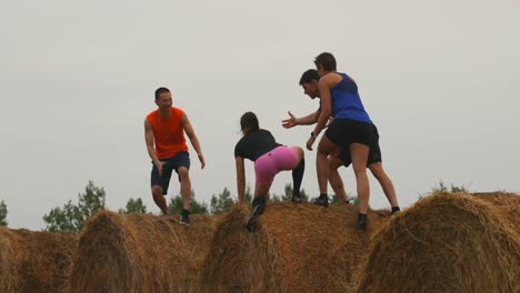 Rear-view-of-fit-mixed-race-friends-helping-a-man-while-jumping-from-hay-bales-4k