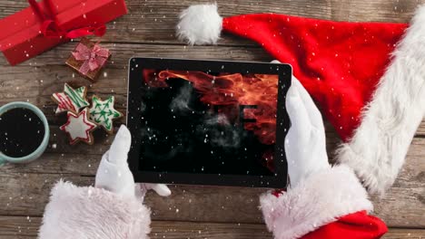 Video-composition-with-snow-over-desk--with-santa-hand-on-tablet