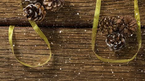 Fallender-Schnee-Mit-Weihnachtlichen-Tannenzapfendekorationen-Auf-Holz