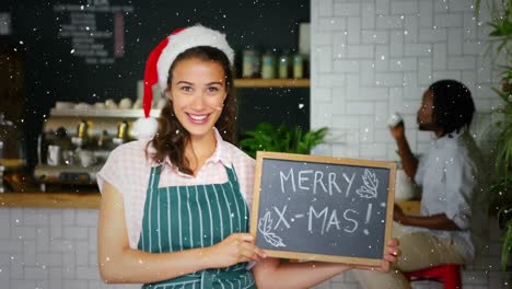Video-composition-with-falling-snow-over-cafe-shop-owner-in-santa-hat-holding-board-with-greetings