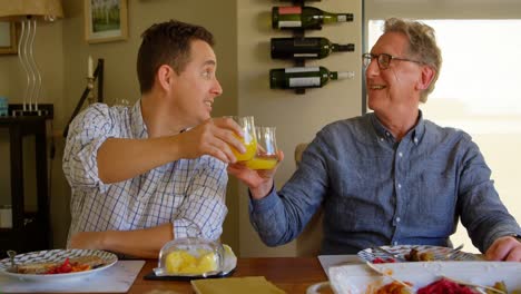 Happy-father-and-son-toasting-glasses-of-juice-at-home-4k