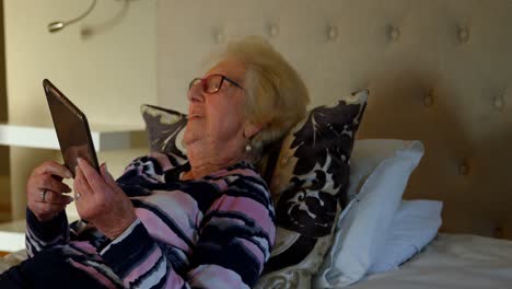 Lächelnde-ältere-Frau-Mit-Digitalem-Tablet-Auf-Dem-Bett-Im-Schlafzimmer-4k