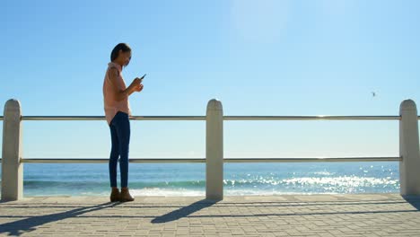 Mujer-Joven-Usando-Teléfono-Móvil-Mientras-Está-De-Pie-En-El-Paseo-Marítimo-4k