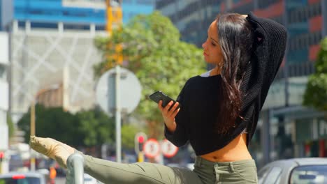 Beautiful-woman-using-mobile-phone-while-leg-stretched-on-a-railings-in-the-city-4k