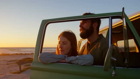 Young-couple-standing-by-van-window-during-sunset-on-beach-4k