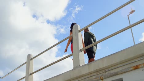 Low-angle-view-of-couple-interacting-with-each-other-while-walking-near-railing-4k