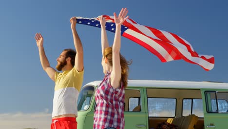 Happy-young-couple-holding-american-flag-on-beach-4k
