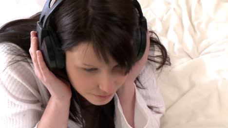 Thoughtful-woman-listening-music-lying-down-on-bed