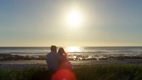 Rear-view-of-romantic-couple-sitting-at-beach-4k
