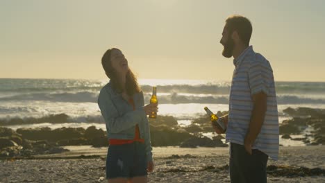 Young-couple-toasting-beer-bottle-at-beach-on-a-sunny-day-4k