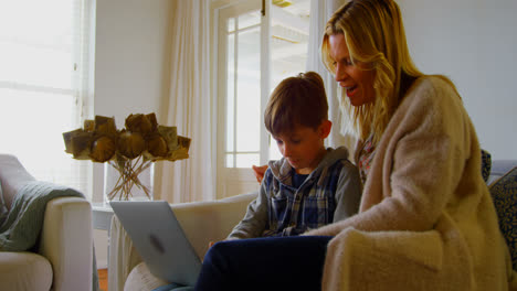 Front-view-of-young-Caucasian-mother-and-son-using-laptop-on-sofa-in-a-comfortable-home-4k