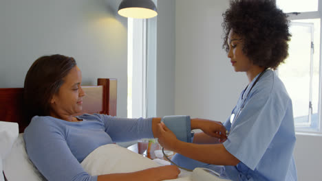 Side-view-of-young-mixed-race-female-doctor-checking-blood-pressure-of-mature-woman-at-home-4k