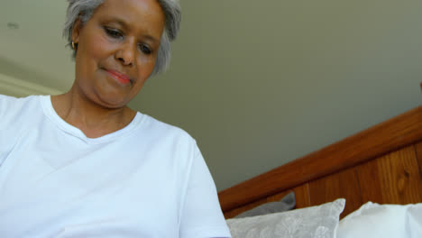 Low-Angle-Ansicht-Einer-älteren-Schwarzen-Frau,-Die-In-Einem-Komfortablen-Zuhause-Auf-Dem-Bett-Sitzt-Und-Ihr-Mobiltelefon-Benutzt,-4K