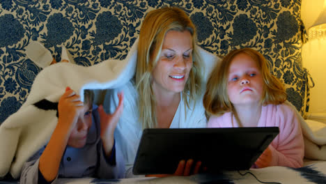 Front-view-of-young-Caucasian-mother-with-her-son-and-daughter-using-digital-tablet-on-bed-in-bedroo