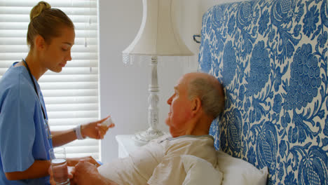 Side-view-of-young-Caucasian-female-doctor-discussing-medication-with-senior-man-on-bed-at-home-4k