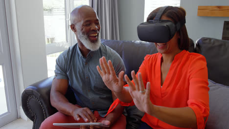 Front-view-of-mature-black-woman-gesturing-and-using-virtual-reality-headset-in-comfortable-home-4k