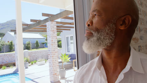 Side-view-of-thoughtful-mature-black-man-standing-near-window-in-a-comfortable-home-4k