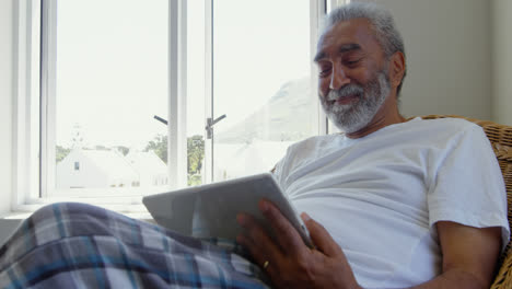 Vorderansicht-Eines-älteren-Schwarzen-Mannes,-Der-Auf-Der-Couch-Sitzt-Und-Ein-Digitales-Tablet-In-Einem-Komfortablen-Zuhause-In-4K-Verwendet