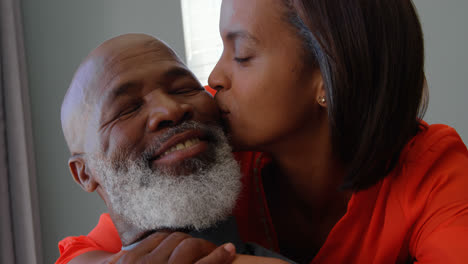 Front-view-of-mature-black-woman-kissing-on-mans-cheek-in-a-comfortable-home-4k