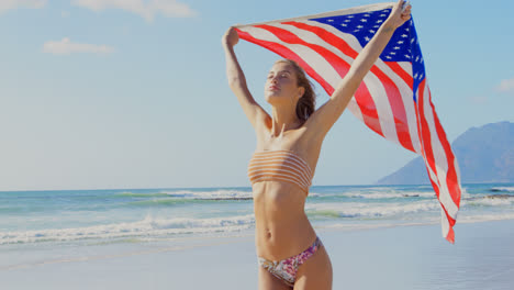 Front-view-of-young-Caucasian-woman-holding-a-American-flag-on-the-beach-4k