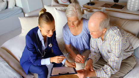 High-angle-view-of-Caucasian-senior-couple-discussing-over-clipboard-with-female-doctor-at-comfortab